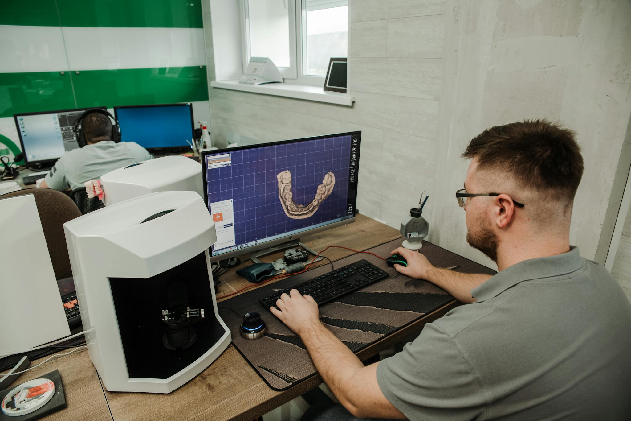 Side view of anonymous male programmer sitting at table and working on computer during creating 3d model of denture in modern dental laboratory